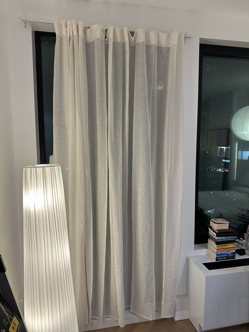 Sheer floor-to-ceiling curtains hung on a window, lit at night
