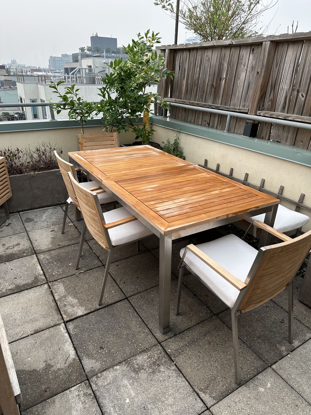 Assembled teak outdoor dining table and cushioned chairs on a rooftop patio