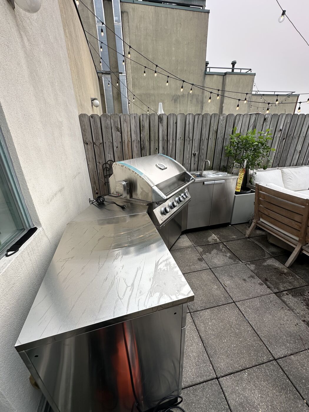 Finished rooftop outdoor kitchen with built-in grill, stainless cabinets, and the NYC skyline behind it