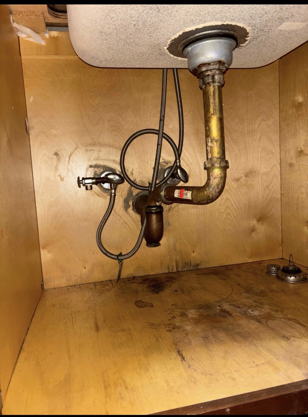 Under-sink plumbing repair showing supply lines and P-trap before replacement