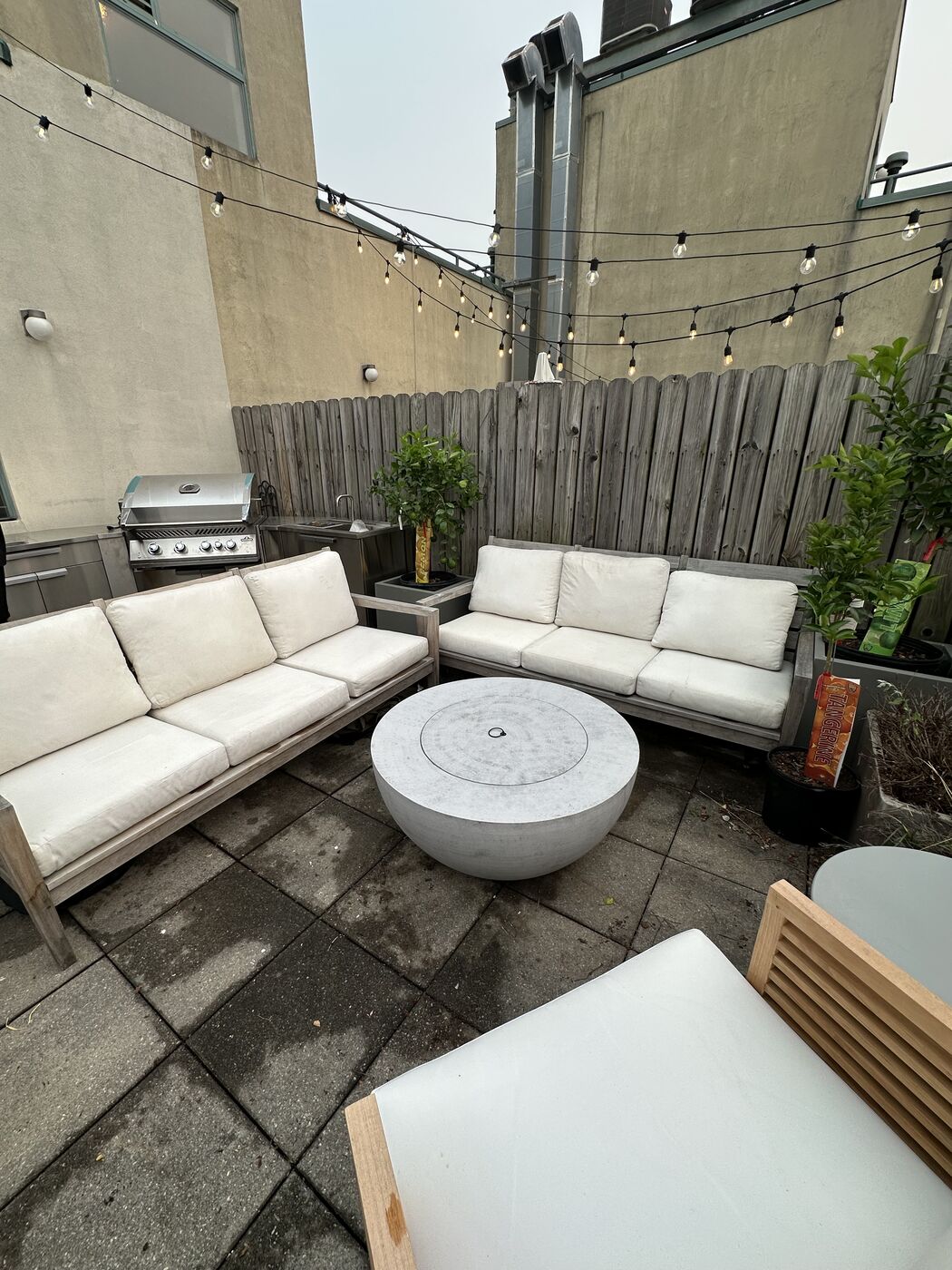 Rooftop lounge with white outdoor sofas, a fire pit table, and string lights set up against the skyline